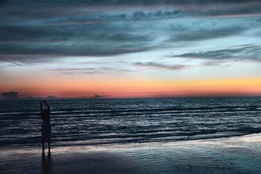 A person stretching at a beach in the evening